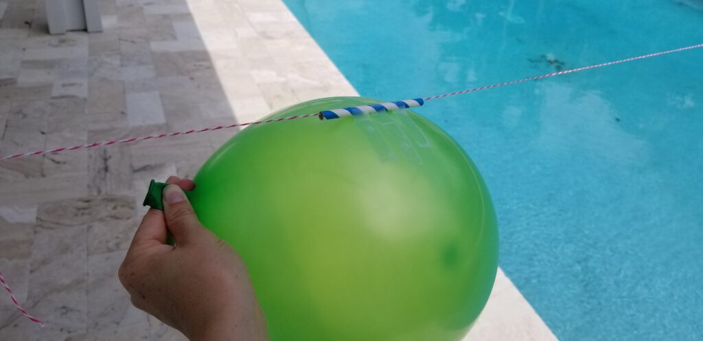 straw with string inside taped to balloon being held by hand