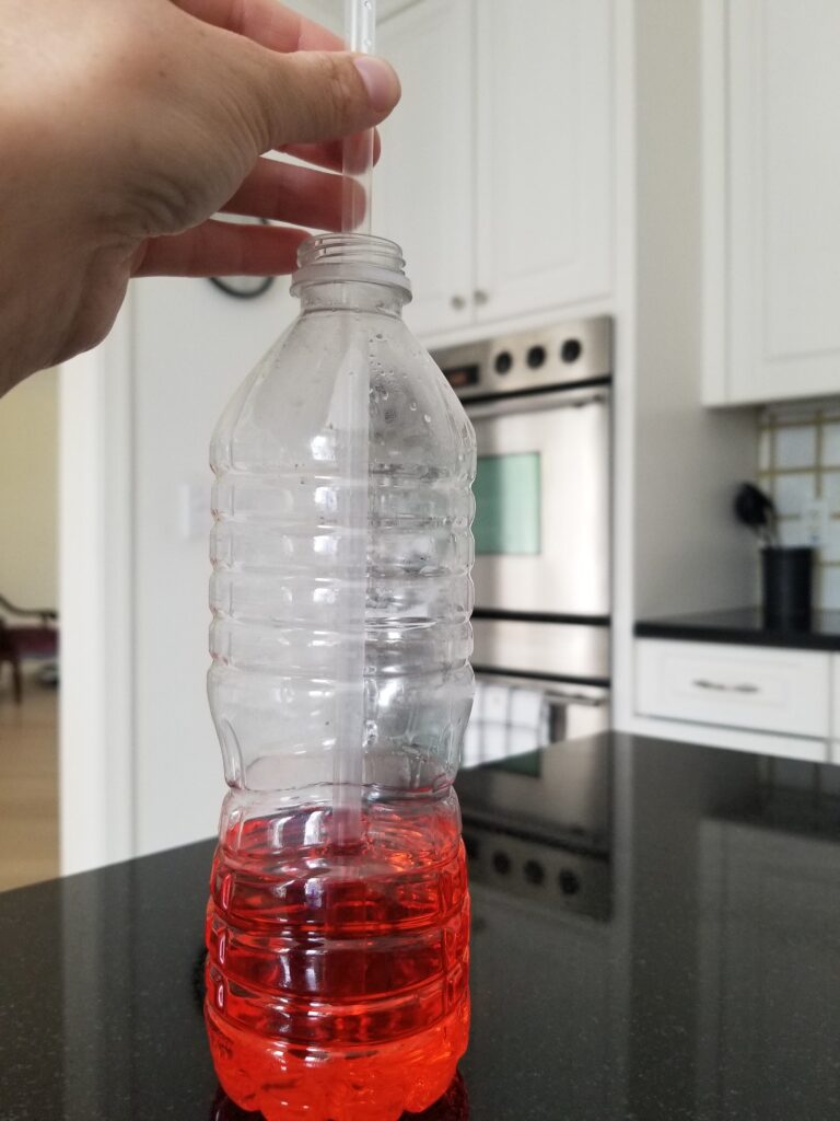 placing a plastic straw into plastic bottle with red liquid