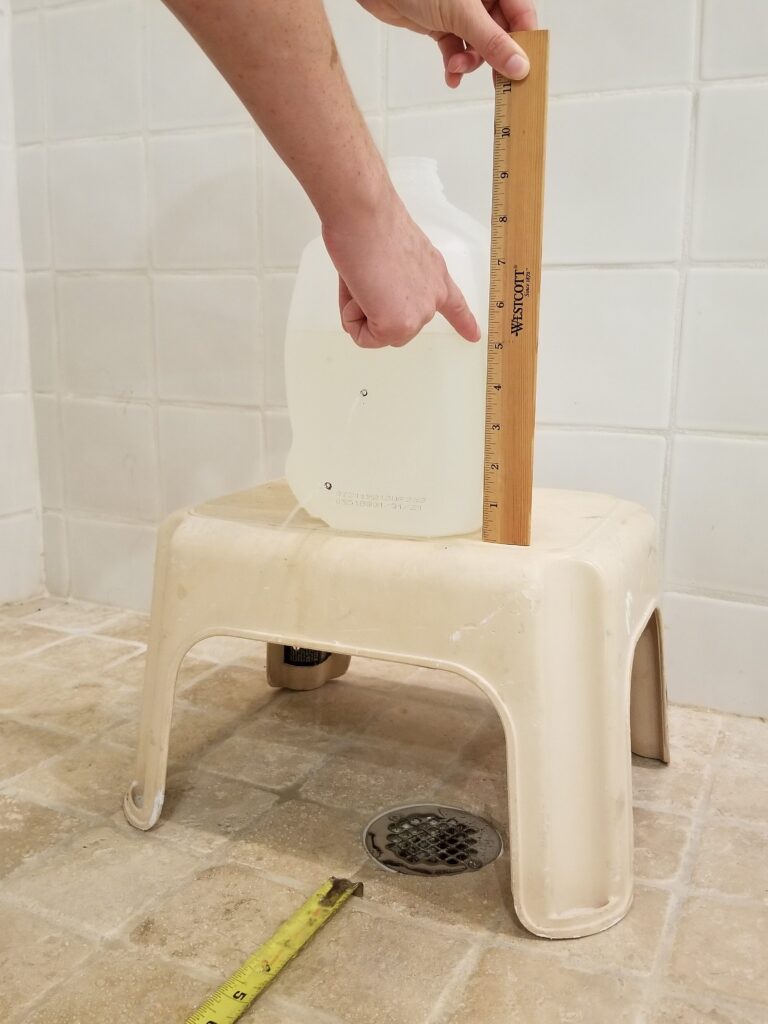 Hand pointing to a ruler that is measuring the height of the water reservoir in the jug.