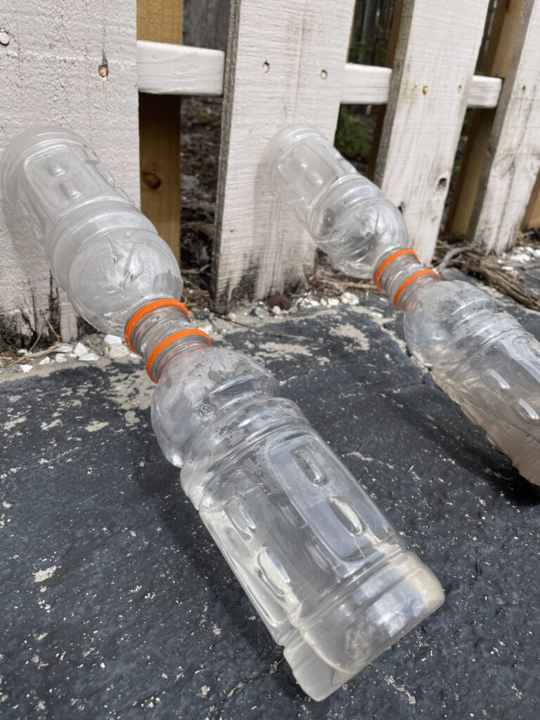 two bottles glued together leaning on fence