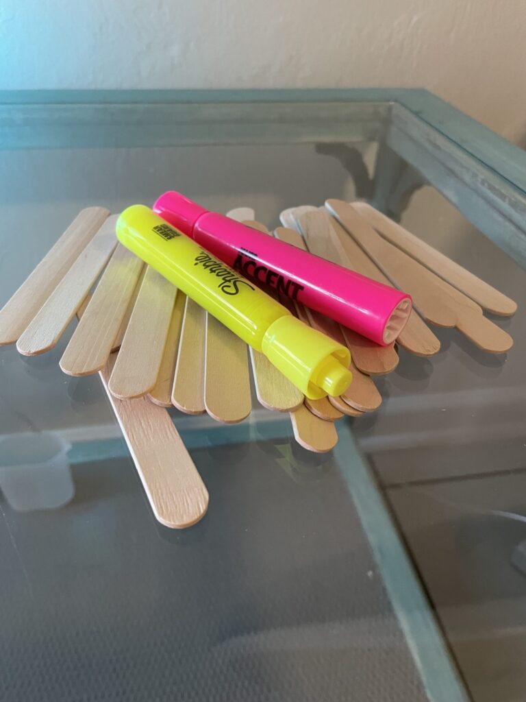Experiment materials are shown on a table including popsicle sticks and highlighter markers.