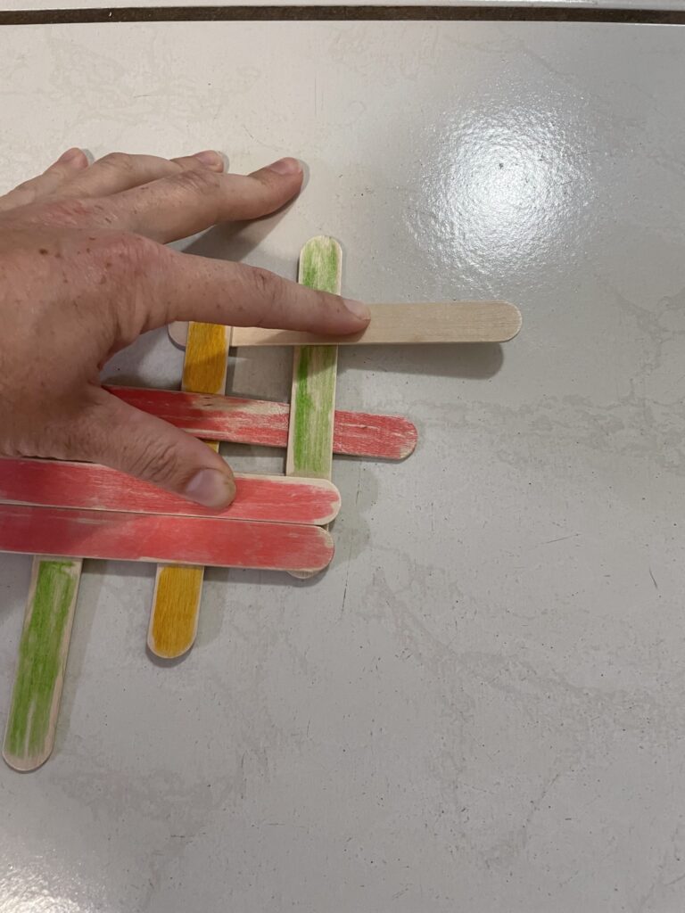 Hand assembling a glued chain of colored popsicle sticks.