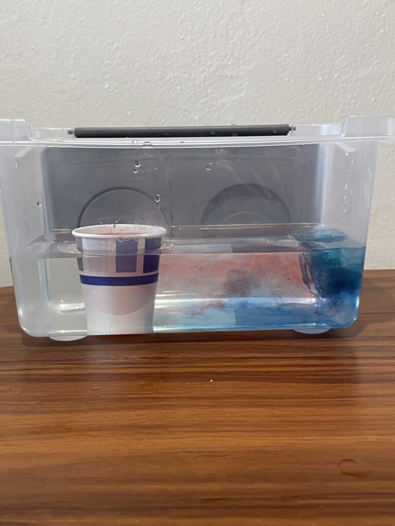 Cup of red water diluting into a water bath